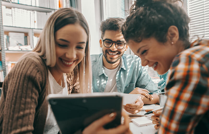 A bunch of college kids laughing at something on a tablet