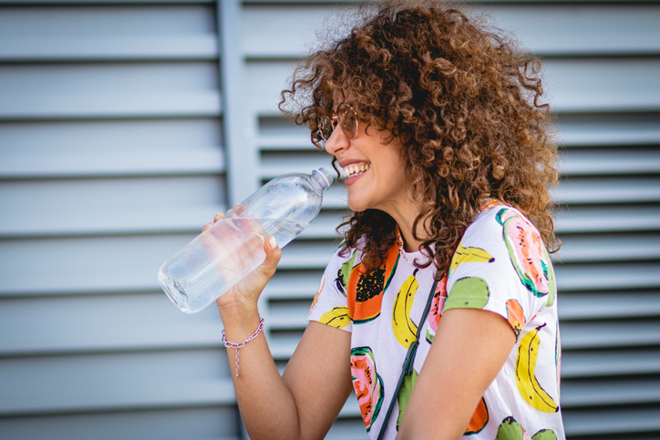 a young woman drinking water from a bottle on the street