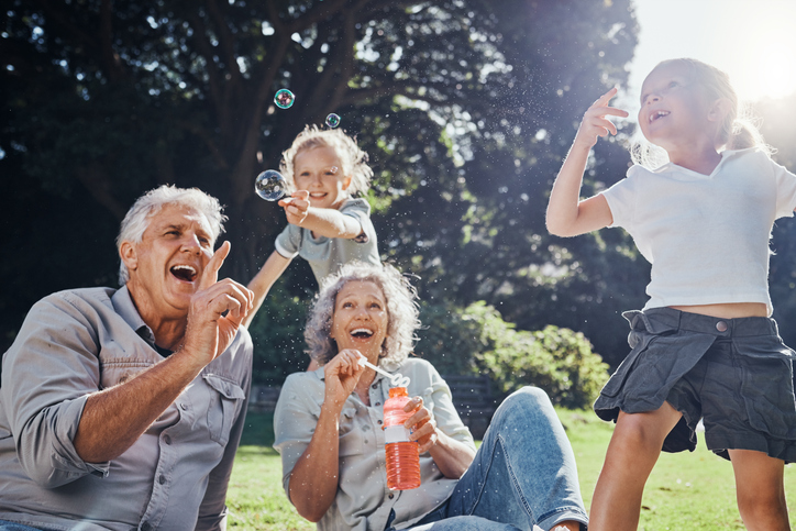 Grandparents, bubbles and children play in park happy together for fun, joy and outdoor happiness. Retired, smile and excited elderly senior couple, girl grandkids and love playing outside in nature