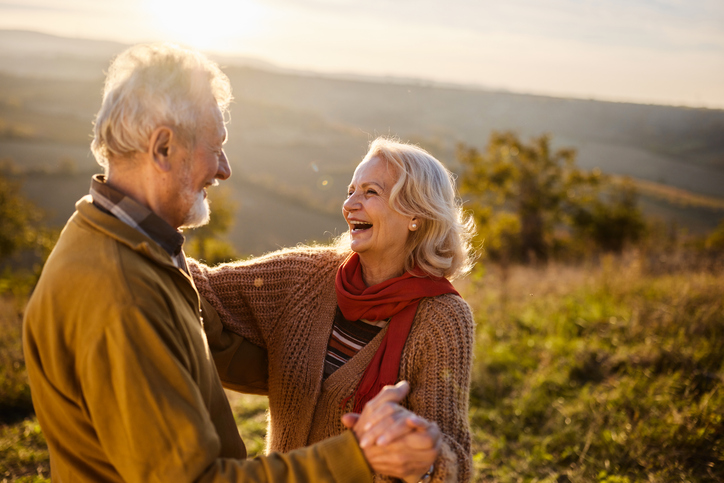 Happy mature couple having fun while dancing during autumn day on a hill. Copy space.