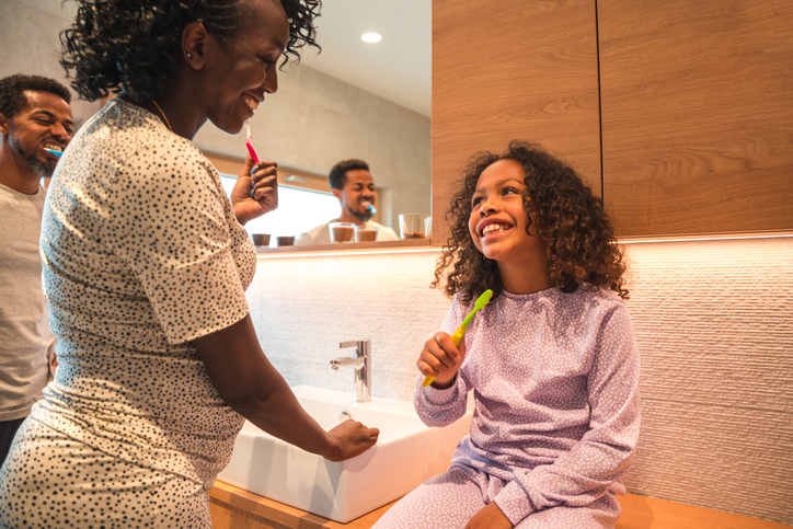 Beautiful African American pregnant female with her family in the bathroom. They are wearing pijamas on an easy Sunday morning. They are smiling and having fun.