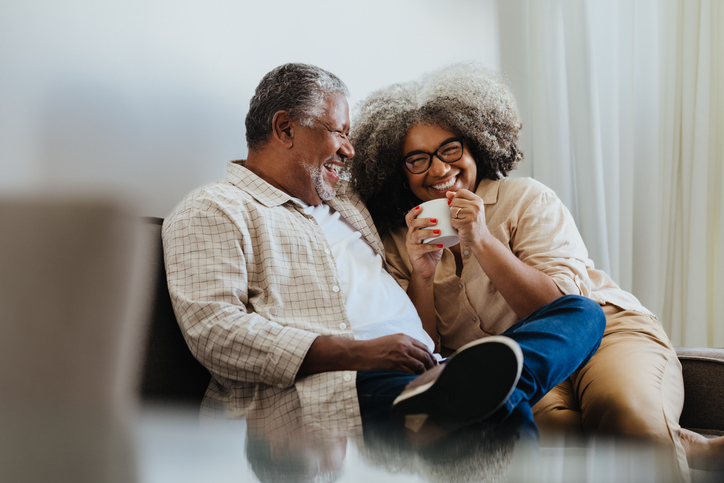 Happy senior couple sitting comfortably and enjoying coffee at home, sharing a joyful moment filled with love and laughter.