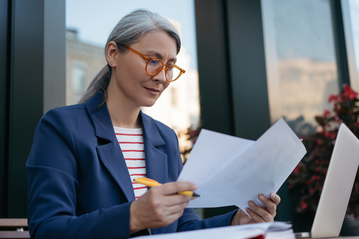 Pensive mature businesswoman reading contract, planning project, brainstorming. Portrait of attractive asian secretary reading, working with documents, sitting at workplace