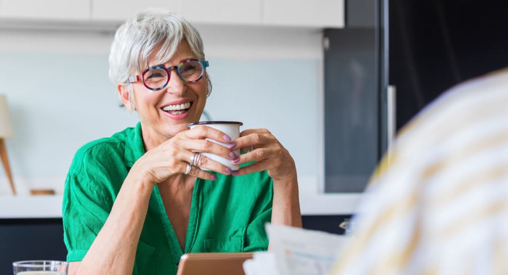 senior woman and handsome senior man sitting at table at home, drinking coffee and talking, having nice time together